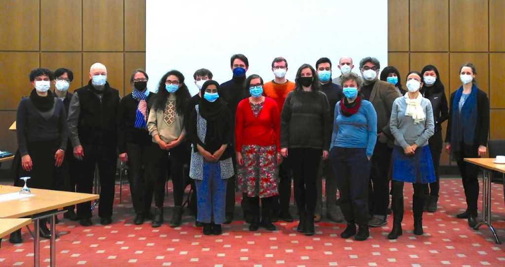 The image shows 19 people positioned for a group photo in a conference room. All are wearing face masks.